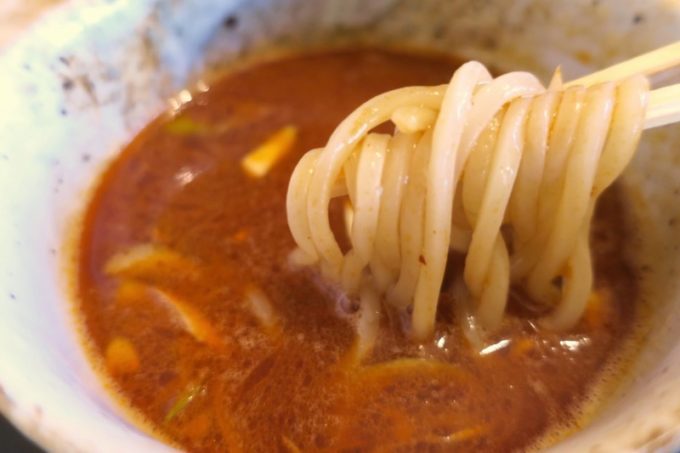 読谷村「麺屋シロサキ」の辛つけめんのつけだれに、麺を浸してすする。